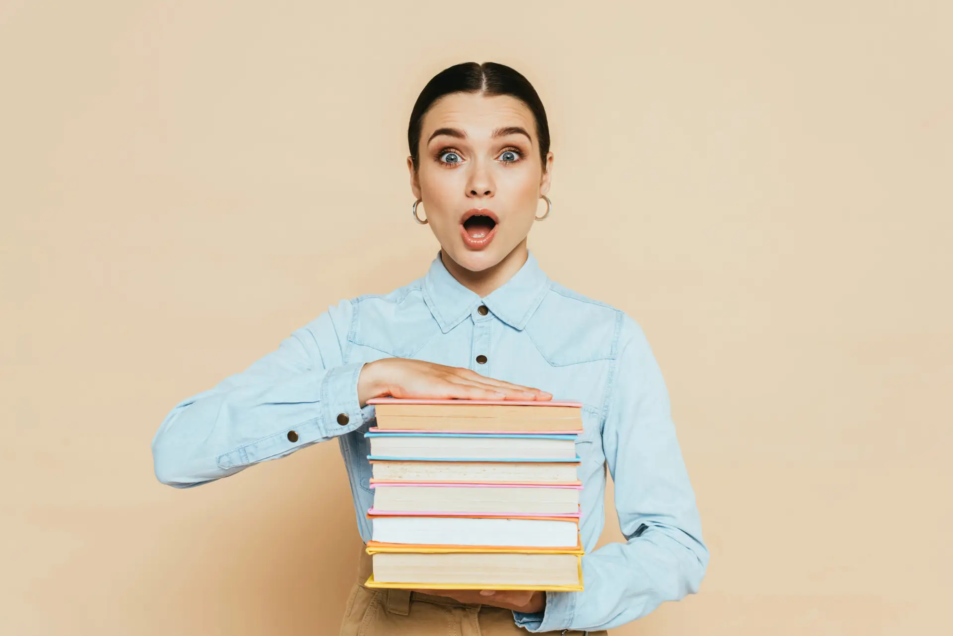 Shocked student in denim shirt with books on beige